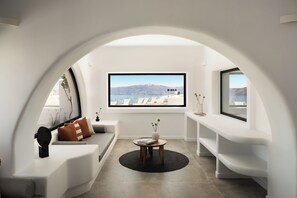 A modern interior with a curved white arch, a sofa, a coffee table, and a view of a mountainous landscape through large windows. - The Duchess (Therasia)