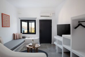A compact living space with a sofa, a small round table, a television, and a door. - The Duchess (Therasia)