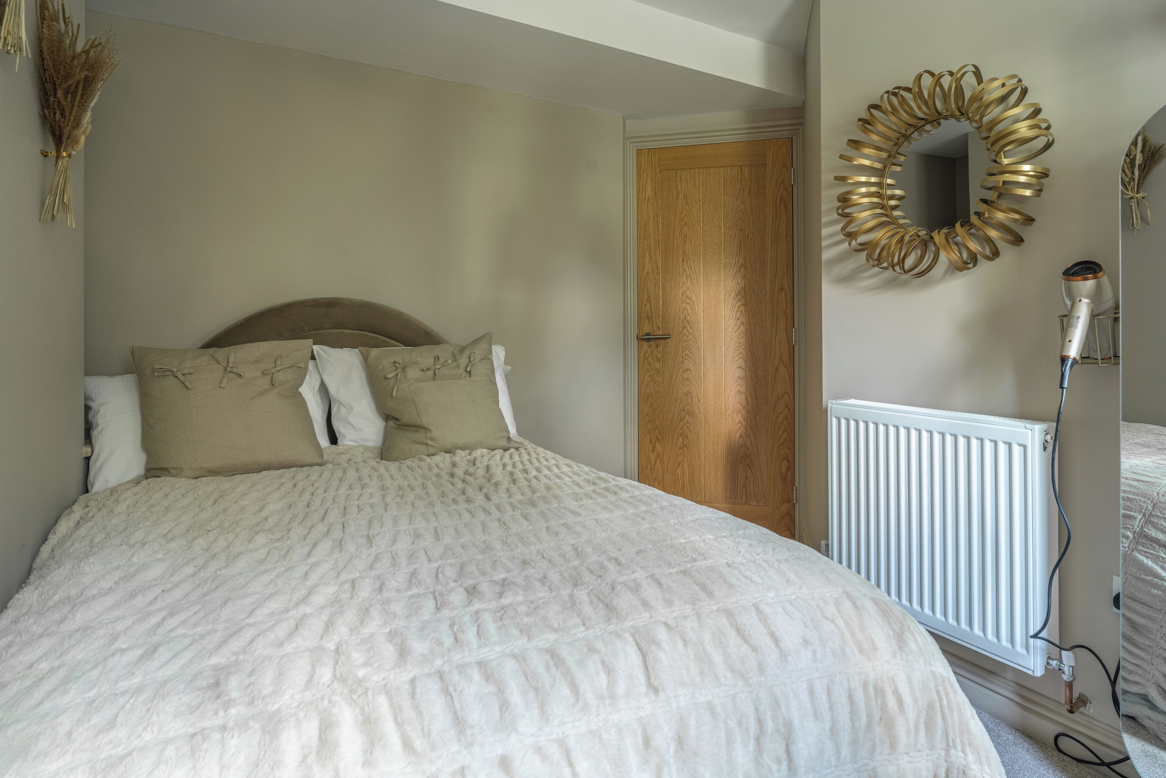 A bedroom with a large bed, a wooden door, a radiator, and a wall-mounted mirror.