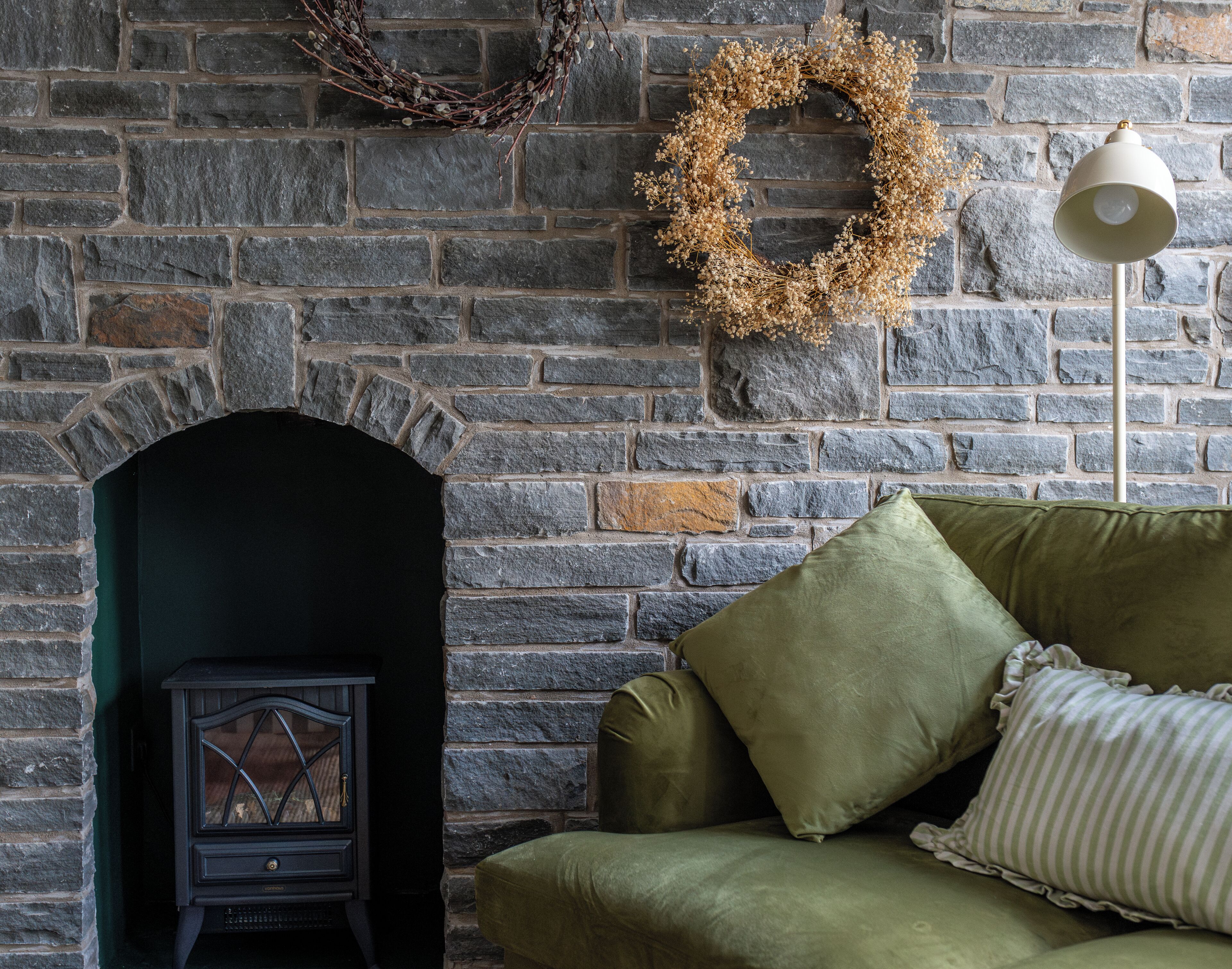 A stone fireplace with a decorative wreath, a vintage radio, and a green sofa with pillows.