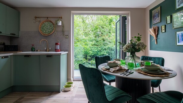 Une cuisine moderne dotée d’un îlot central, de chaises vertes et d’une table à manger prévue pour quatre personnes.
