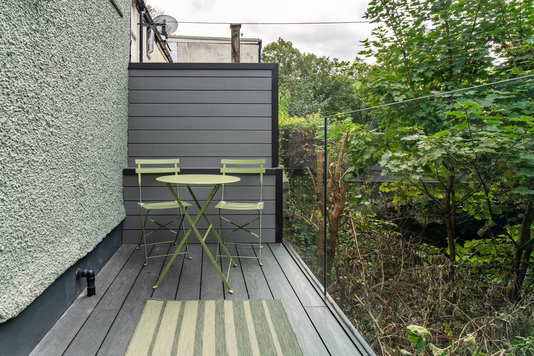 A small outdoor patio with a table and chairs, surrounded by greenery.