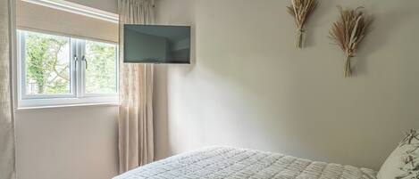 Une chambre à coucher avec un lit, un téléviseur fixé au mur et une fenêtre avec des rideaux.