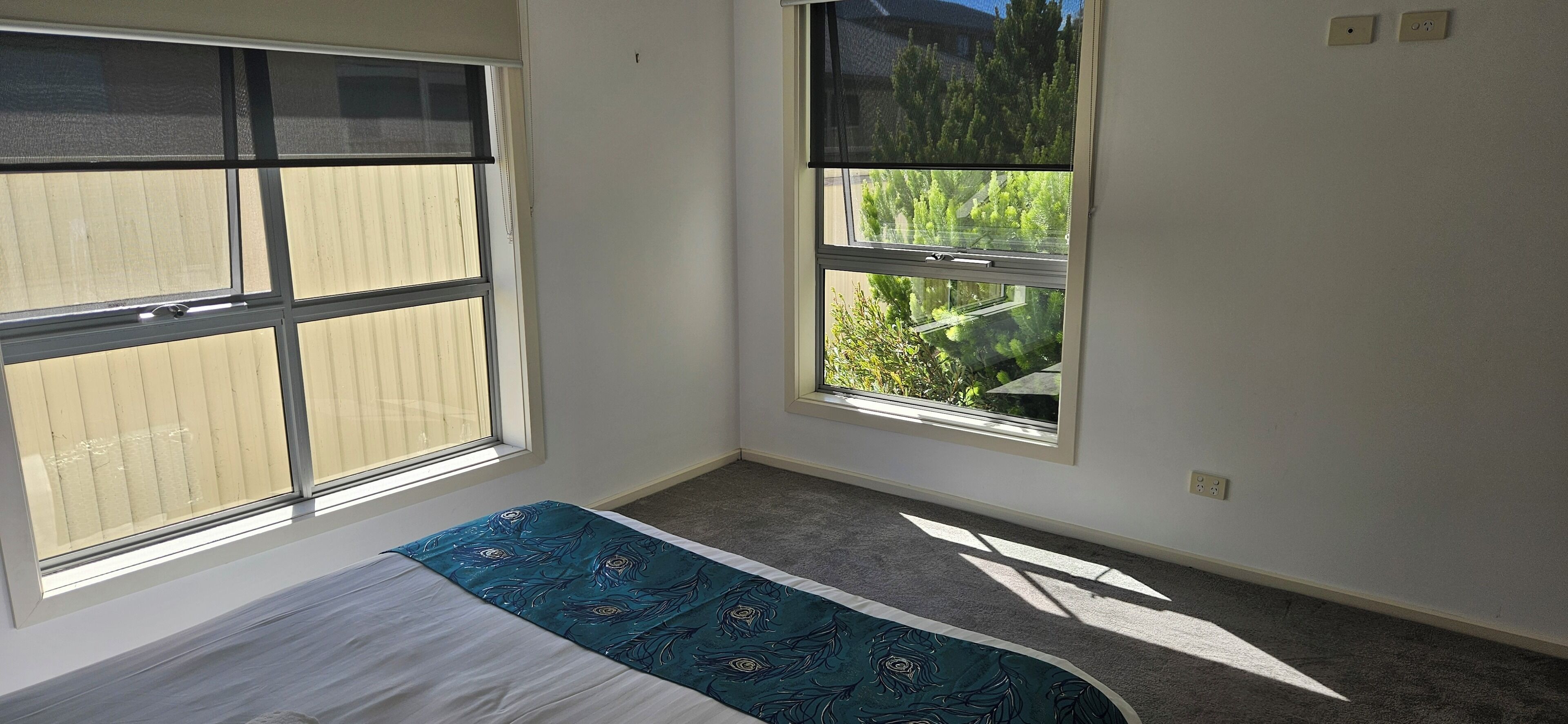 Un dormitorio con una cama, dos ventanas y suelo alfombrado.