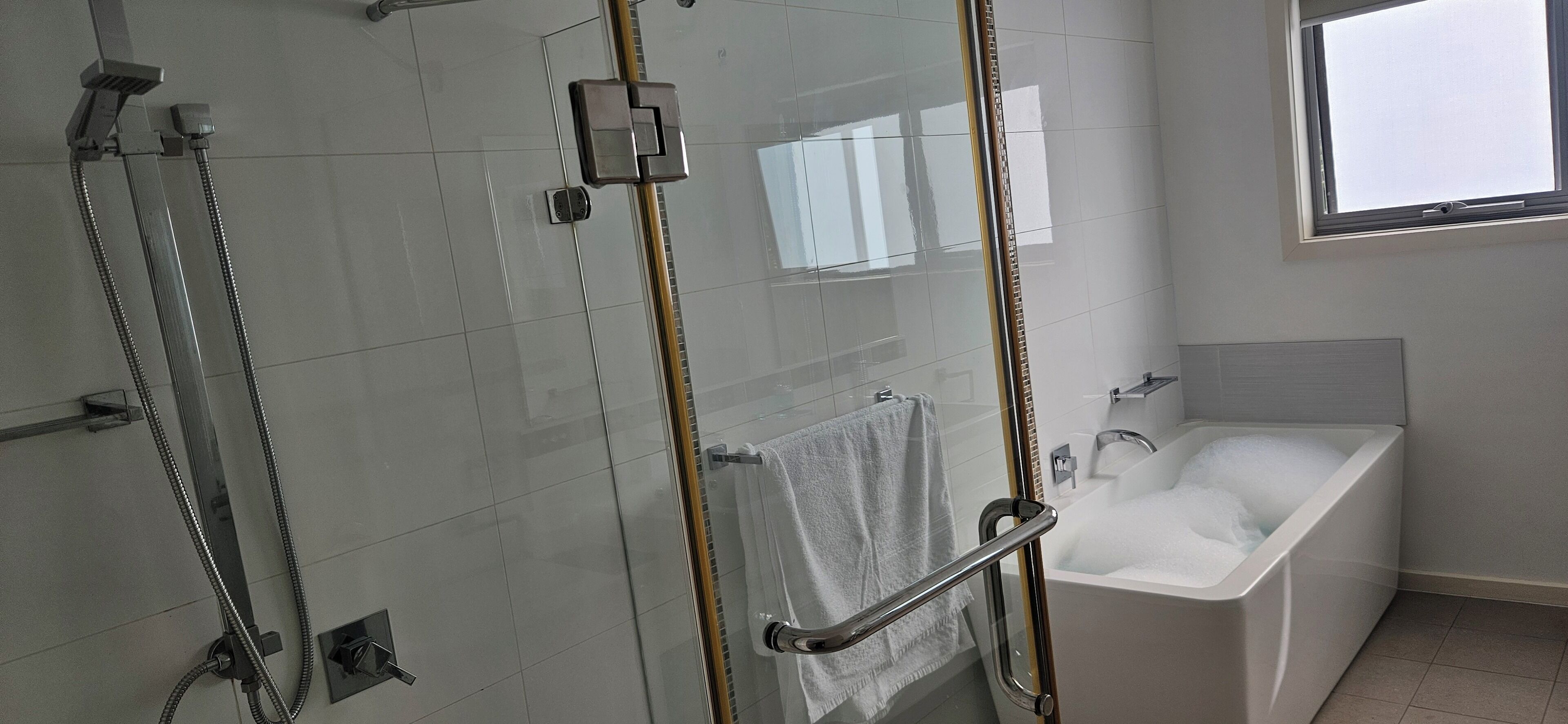 A modern bathroom with a glass-enclosed shower, a white bathtub, and a window providing natural light.