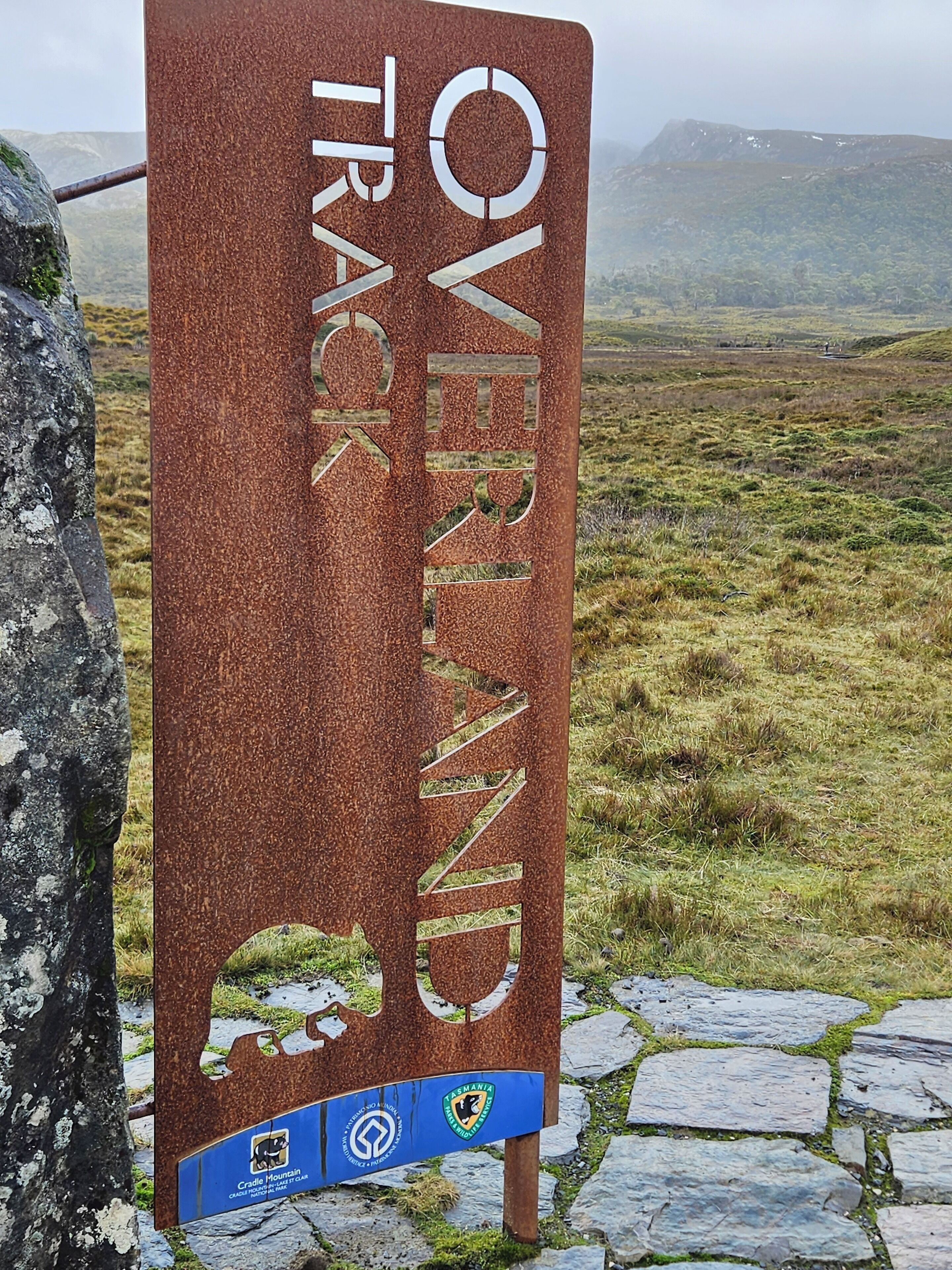 A sign for the Overland Track with a logo and a map of Tasmania.