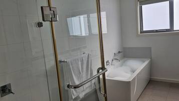 A modern bathroom with a glass shower enclosure, a bathtub, and a window providing natural light.
