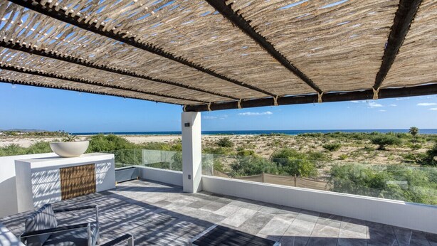Um terraço com vista para o mar, uma área de estar e uma tigela decorativa em um pedestal.