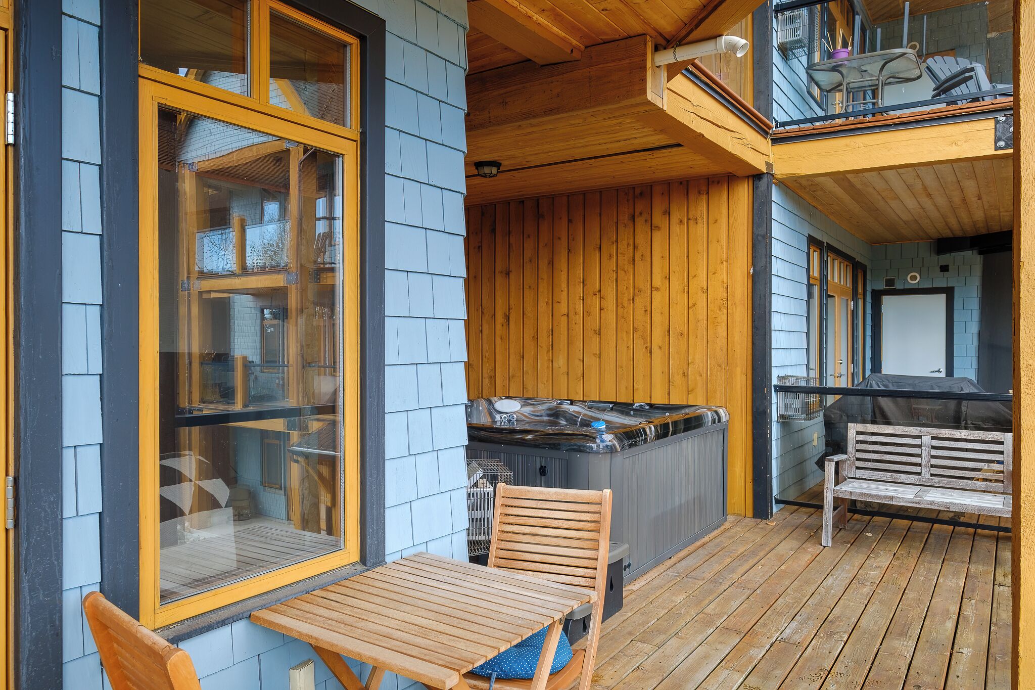 A wooden deck with a hot tub, a table, and a bench.