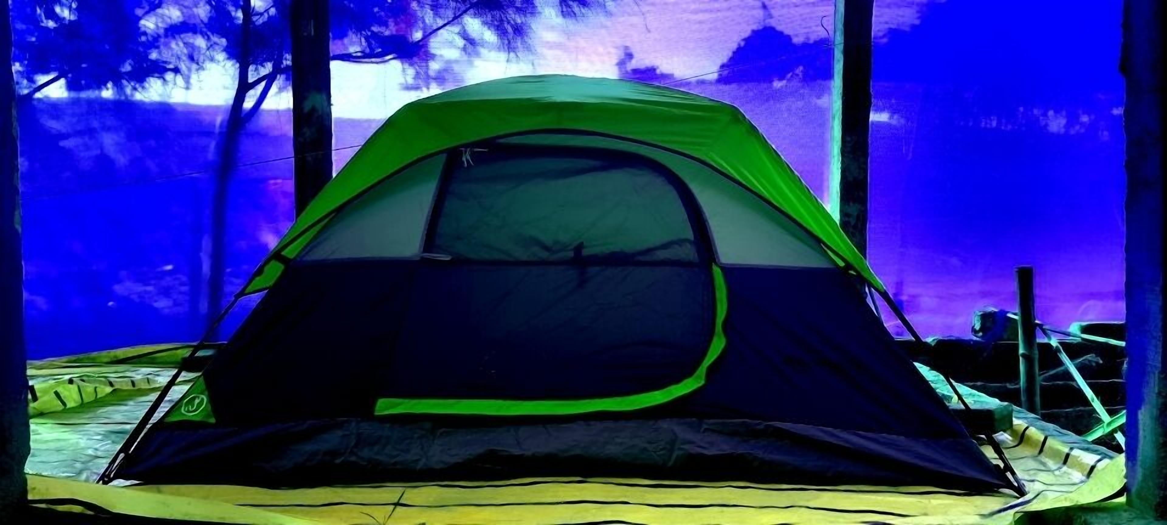 A tent set up in a forested area with trees in the background.