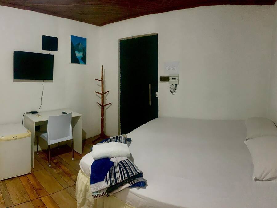 A small, simple room with a bed, a desk, a chair, a mirror, and a TV.
