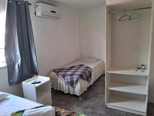Una habitación pequeña y funcional con cama, mesita de noche, armario y ventana con cortina.