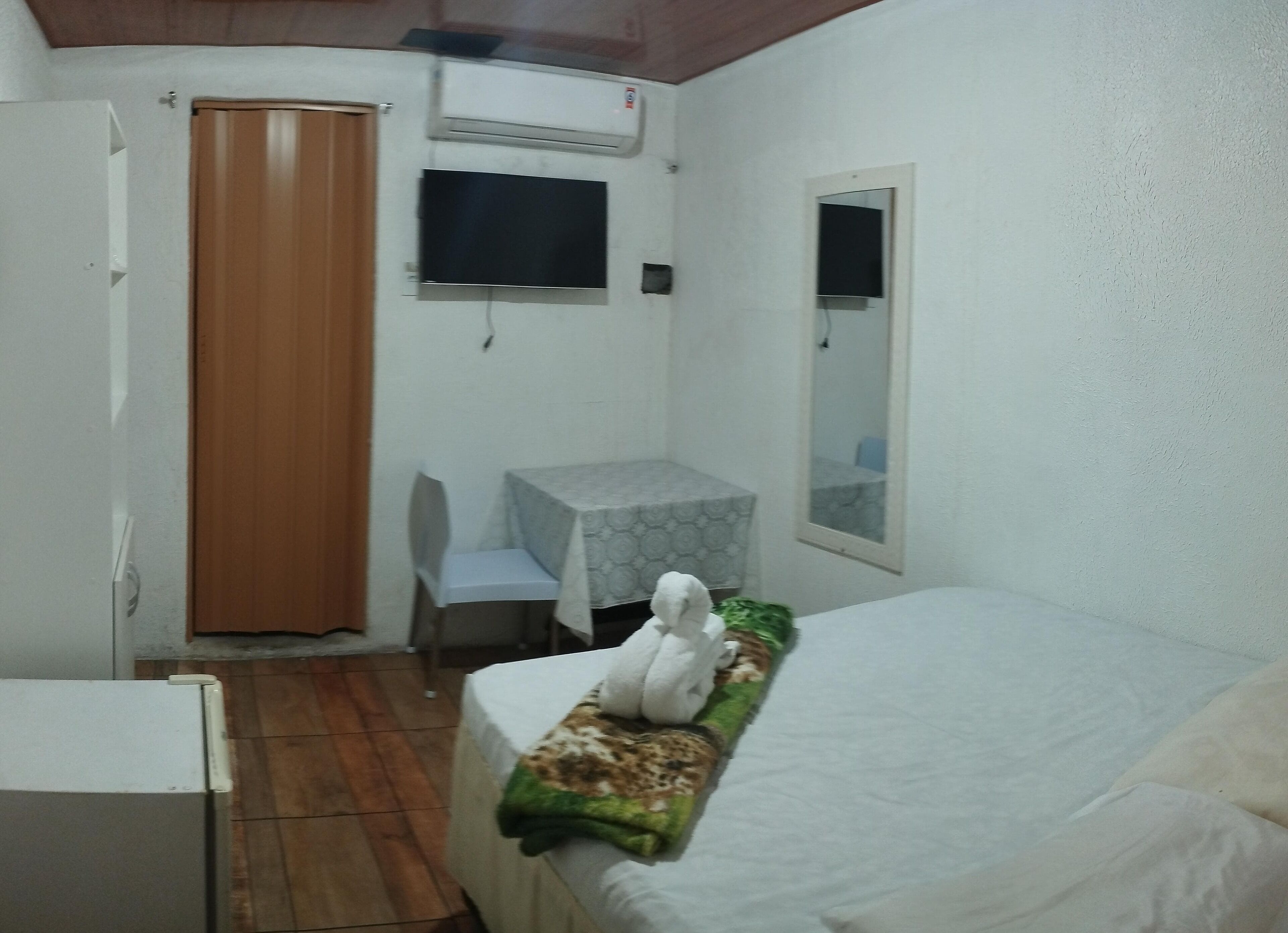 Una habitación pequeña y funcional con cama, escritorio con silla, armario y unidad de aire acondicionado.