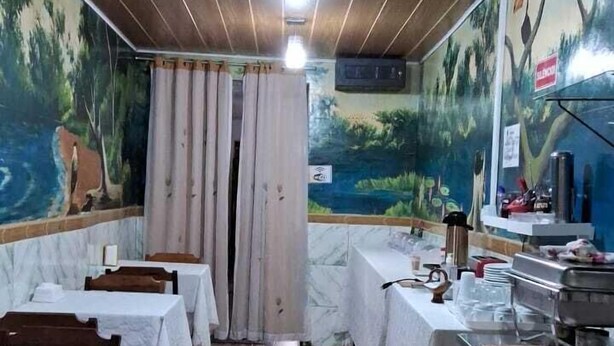 Un restaurante con paneles de techo de madera, suelo de baldosas y mesas cubiertas con manteles blancos.