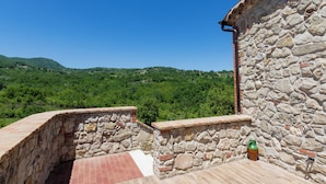 A stone building with a tiled roof overlooking a green landscape.