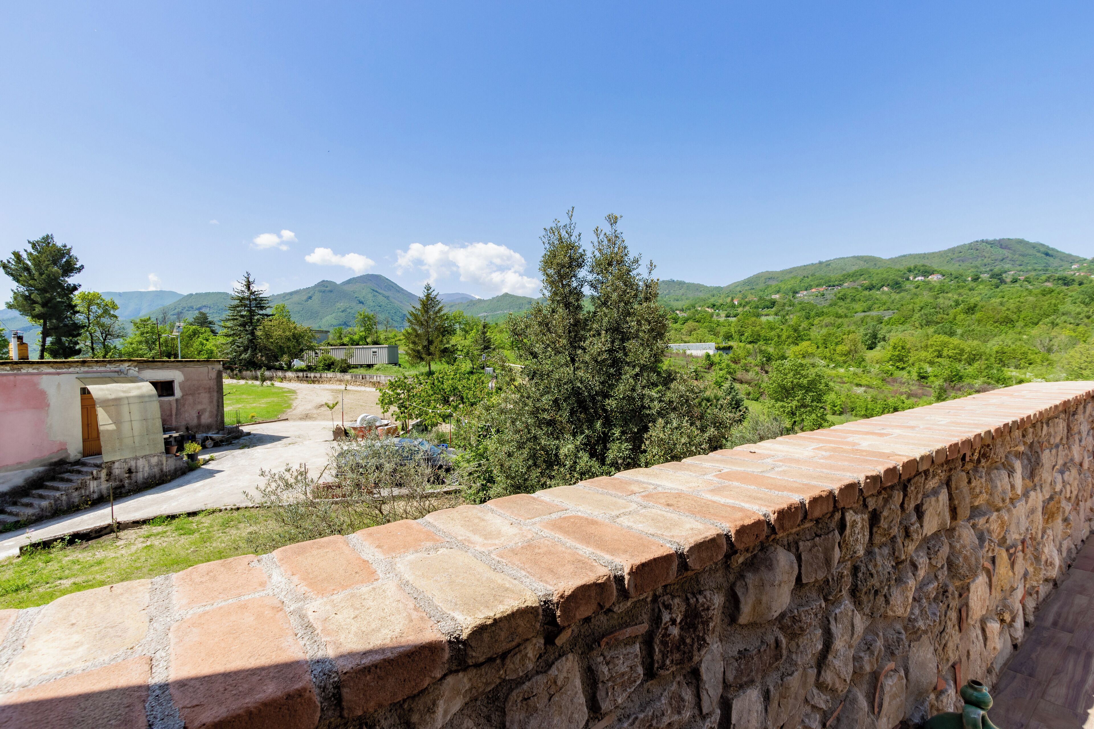 A stone wall with a view of a green landscape and mountains in the distance.