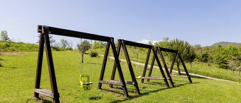 A row of wooden swing sets in a grassy field with a clear sky.