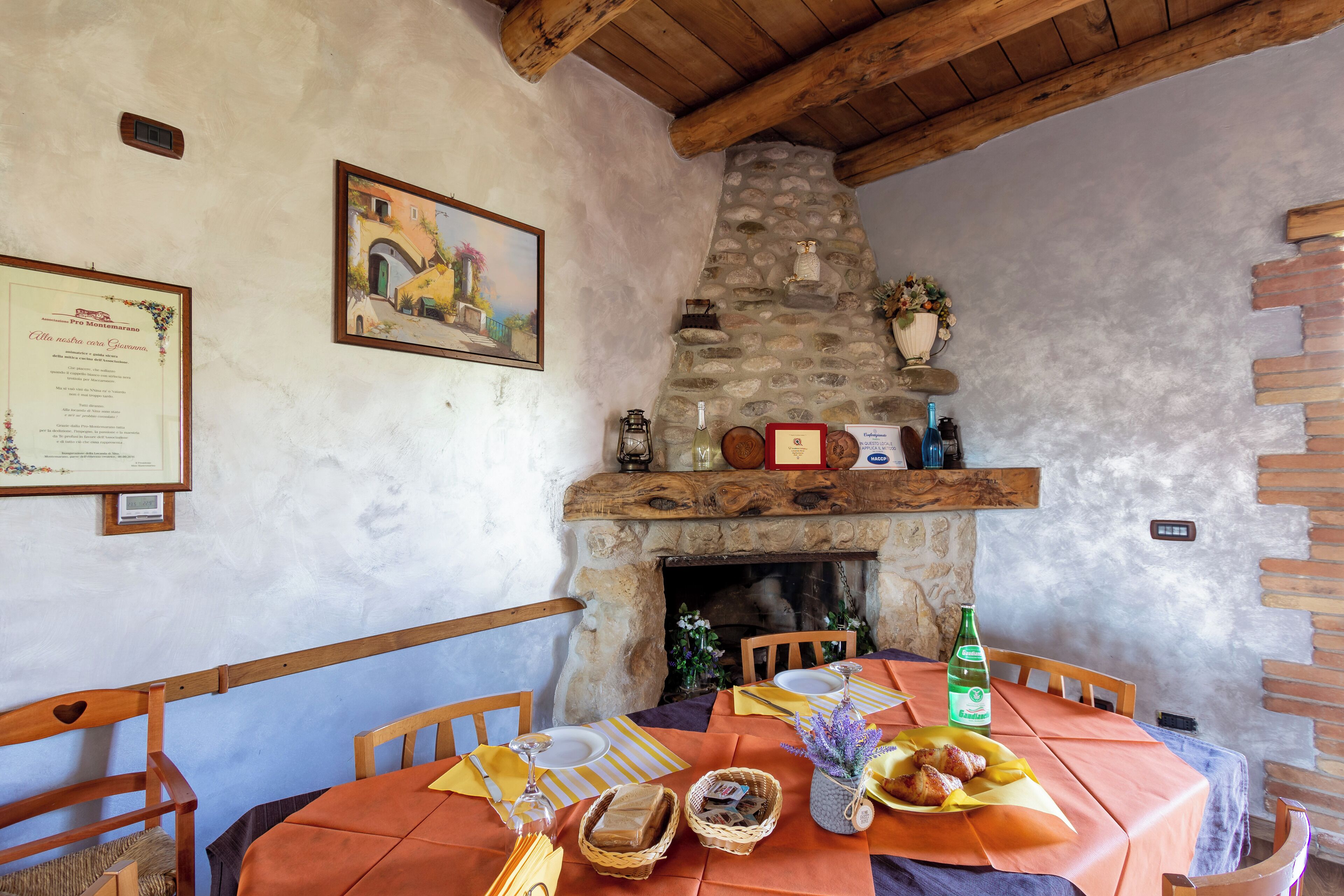 A rustic dining area with a stone fireplace, wooden beams, and a table set for a meal.