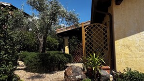 A courtyard with a stone pathway, a wooden gate, and a variety of plants and rocks. - Villetta Rosmarino 1700 meters from the wonderful beaches of Chia (Sardegna)