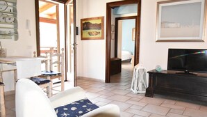 A living room with a white sofa, a television, a wooden cabinet, and a painting on the wall. - Villetta Rosmarino 1700 meters from the wonderful beaches of Chia (Sardegna)
