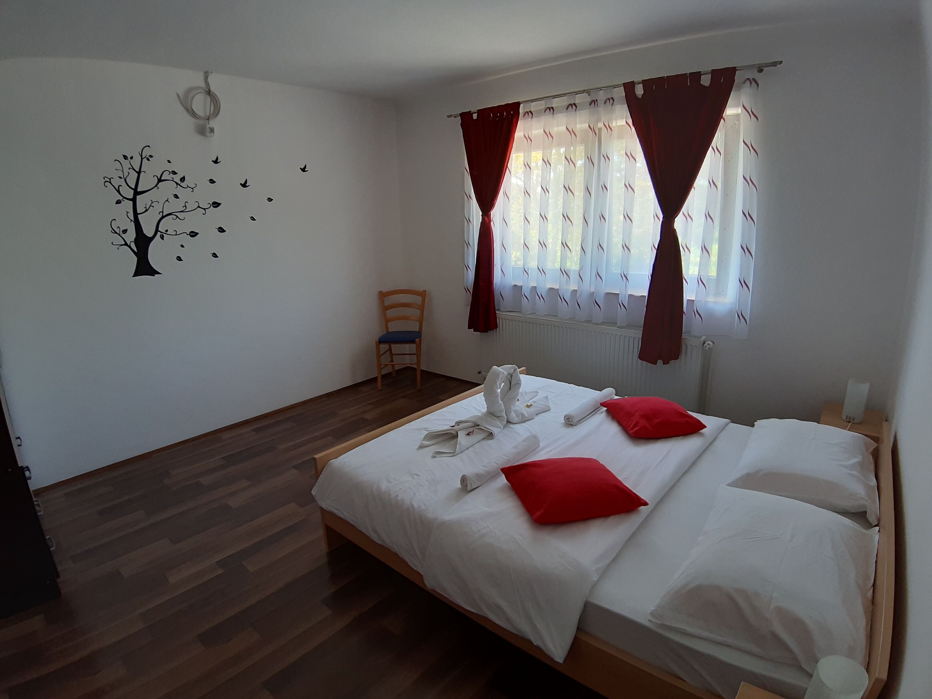 A neatly arranged bedroom with a wooden bed, white bedding, red pillows, and a chair.