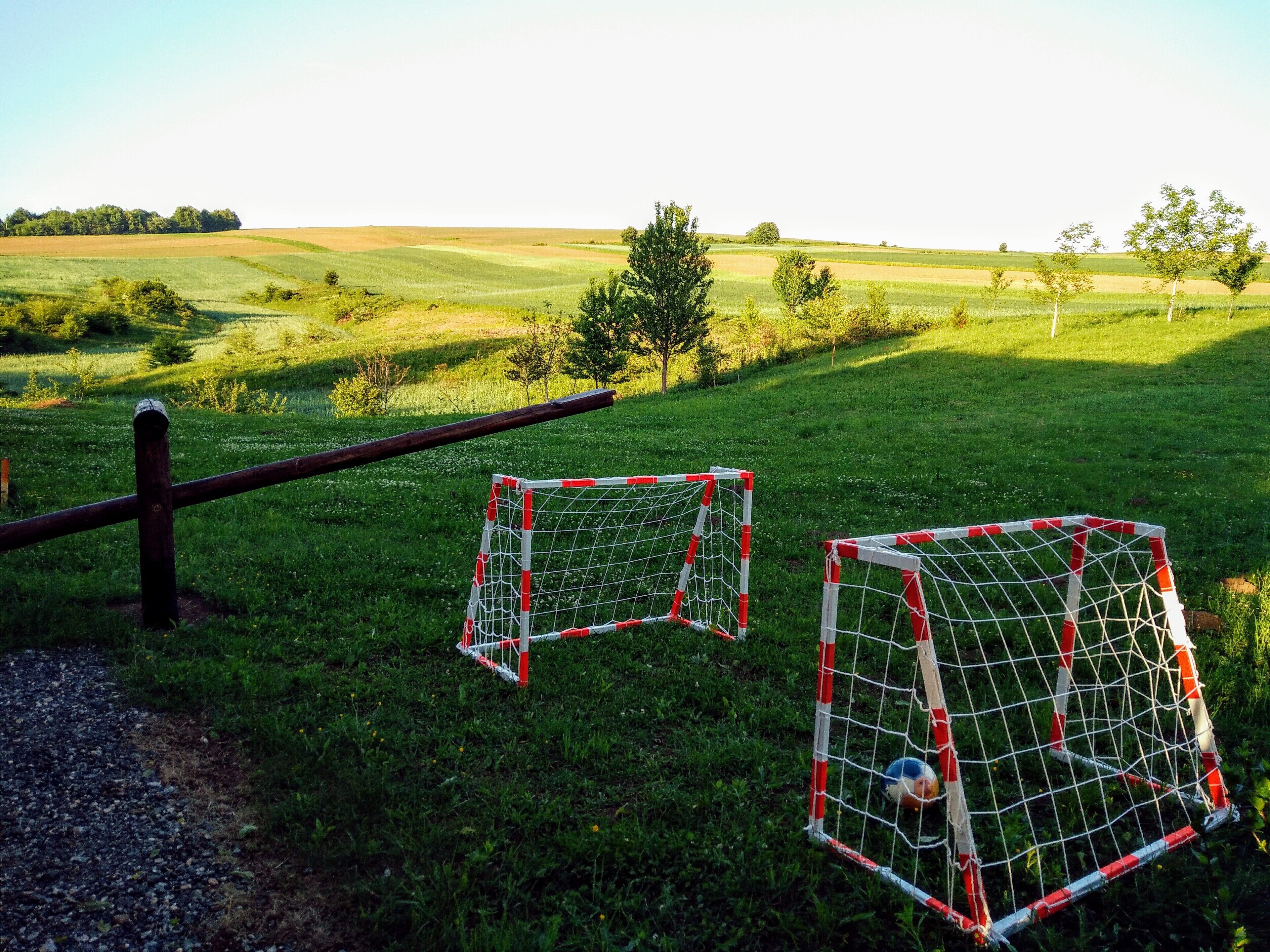 Two soccer goals in a grassy field with a fence in the foreground.