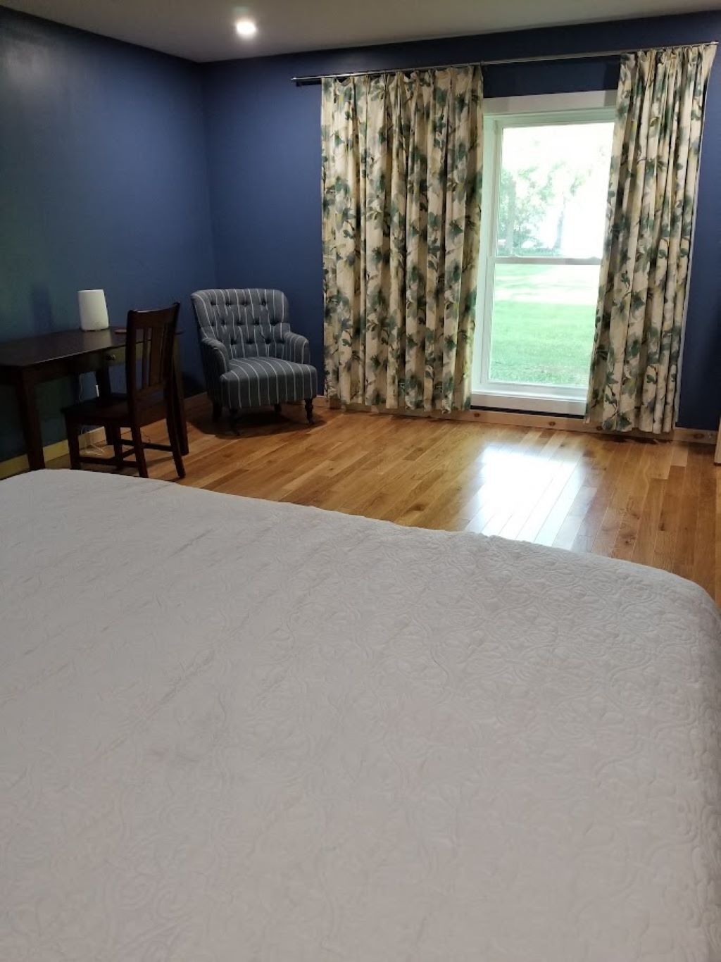 A bedroom with a large bed, a chair, a table, and a window with curtains.