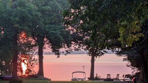 A serene lakeside setting with a covered vehicle and chairs under trees. - LAKEFRONT COMFORT (Chazy)