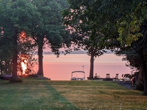 A serene lakeside setting with a covered vehicle and chairs under trees. - LAKEFRONT COMFORT (Chazy)