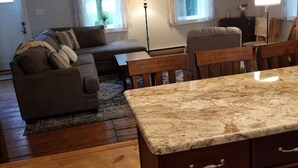 A cozy living room with a sofa, a dining table, and a kitchen area with wooden cabinets. - LAKEFRONT COMFORT (Chazy)