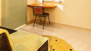 Una habitación pequeña con una puerta verde, un escritorio de madera, una silla y un tapete amarillo tejido.
