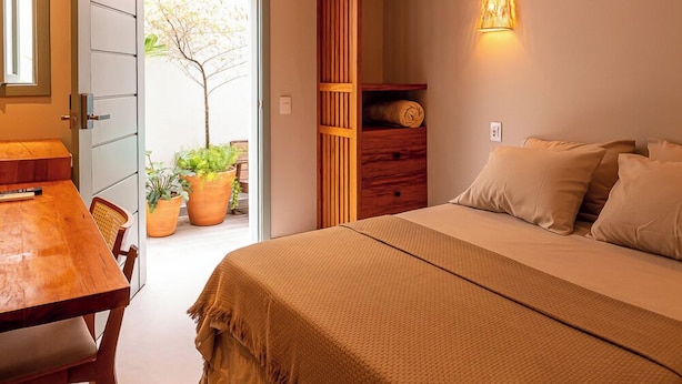 Un dormitorio con cama, mesita de noche y armario de madera. Se ve una puerta que da a un espacio exterior con plantas.