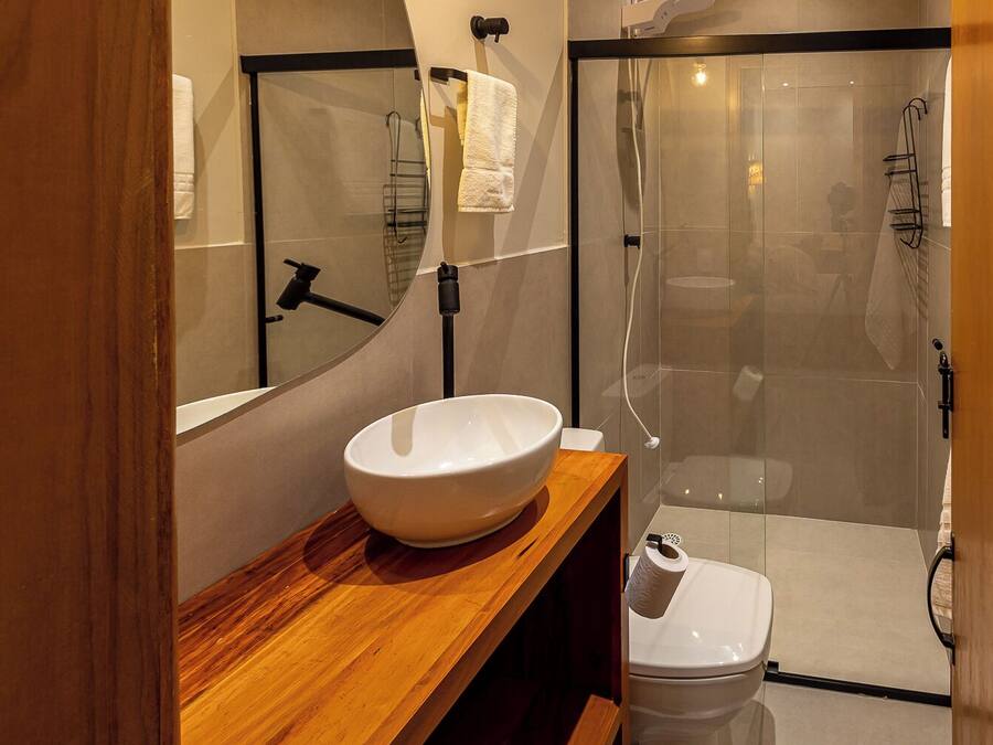 A modern bathroom with a wooden vanity, a white sink, a mirror, and a glass-enclosed shower area.