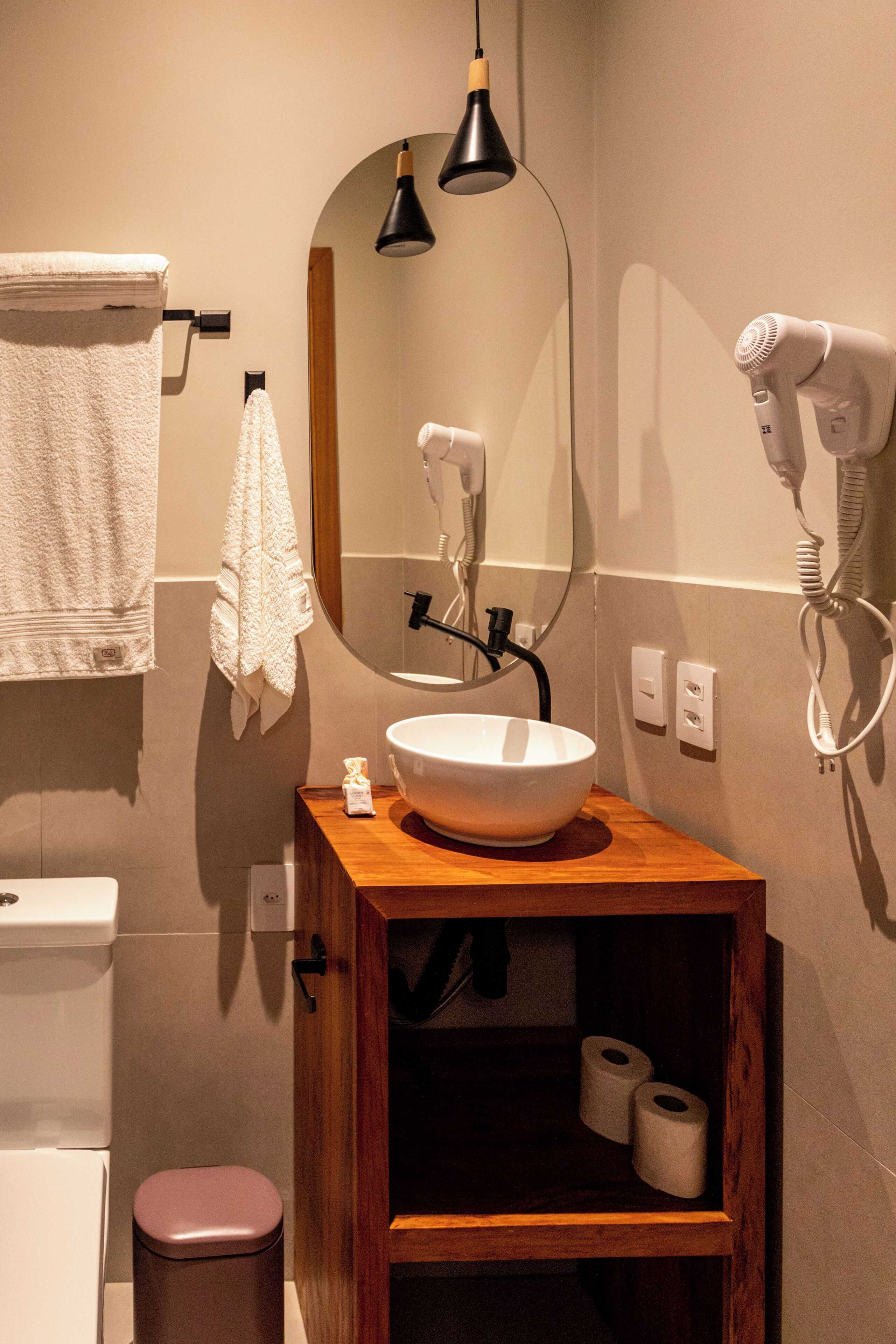 A bathroom with a wooden vanity, a white sink, a mirror, a towel rack, a hairdryer, and a toilet.