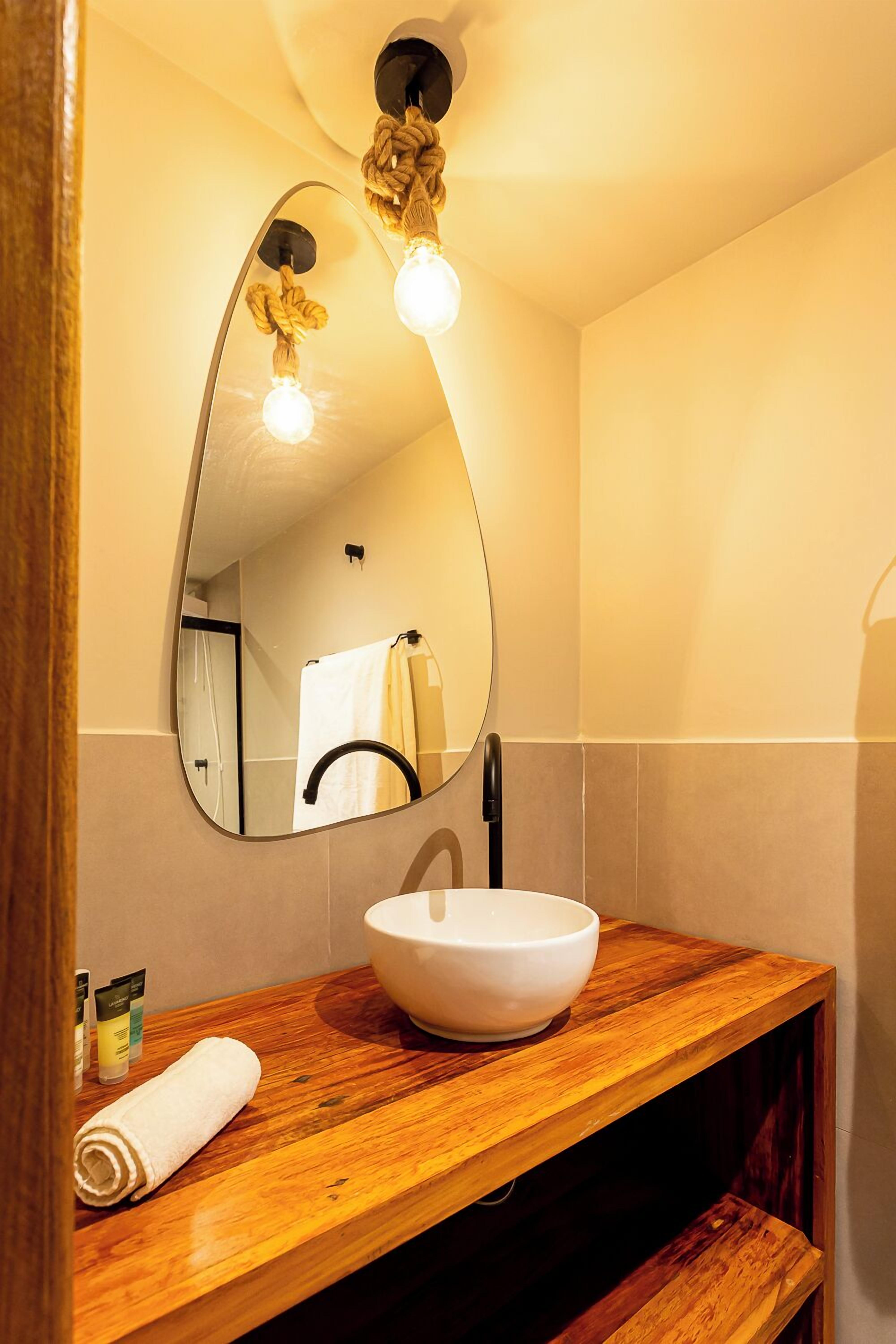 A bathroom with a wooden vanity, a white sink, and a mirror with a rope light fixture.