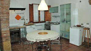 Uma cozinha compacta com uma mesa de jantar redonda, cadeiras transparentes, uma geladeira branca e um lustre.
