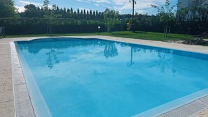 Una piscina rectangular con superficie de agua azul cristalina, rodeada por un patio empedrado.