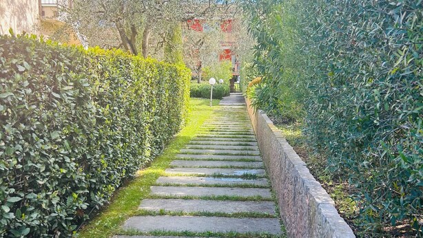Un camino de piedra bordeado por setos cuidados que conduce a un edificio con detalles rojos.