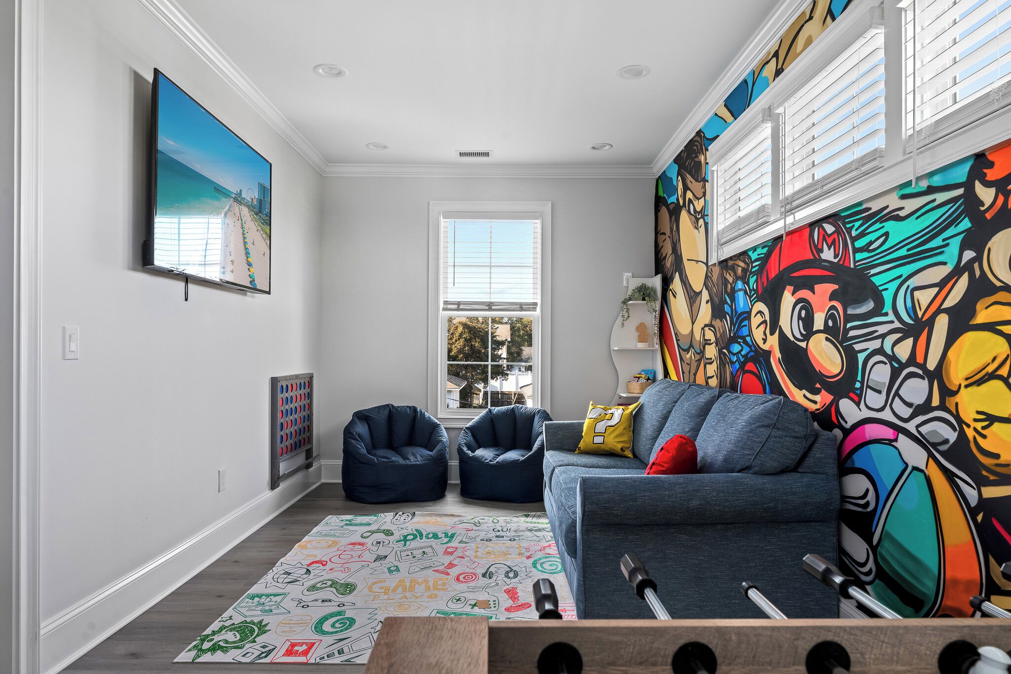 A living room with a large mural, a sofa, bean bags, and a colorful play mat.