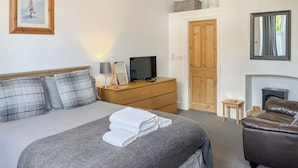 A neatly arranged hotel room with a bed, a television, a dresser, a mirror, and a leather sofa. - Treasure Cove-UK48780 (Whitby)