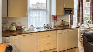 A compact kitchen with a sink, a toaster, and a microwave. There is a window with a view of buildings outside. - Treasure Cove-UK48780 (Whitby)
