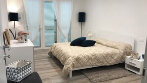 Een slaapkamer met een bed, nachtkastjes, een bureau, een stoel en een raam met jaloezieën.