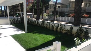 Een verzorgde tuin met een witte omheining, groen gras en bomen.