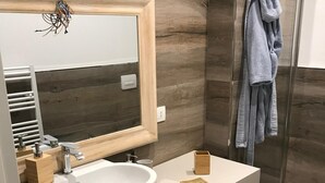 Een moderne badkamer met een groot wit wastafelblad, een houten opbergmeubel en een douchecabine met glazen wanden.