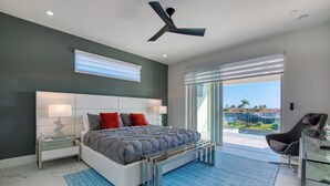 A modern bedroom with a large bed, a ceiling fan, and a view of the outdoors. - VRCC Villa Alany- Luxury Getaway- lastminute deals (Cape Coral)