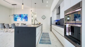 A modern kitchen with a central island, stainless steel appliances, and a dining area with chairs. - VRCC Villa Alany- Luxury Getaway- lastminute deals (Cape Coral)
