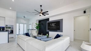 A modern living room with a white sofa, a TV mounted on the wall, and a ceiling fan. - VRCC Villa Alany- Luxury Getaway- lastminute deals (Cape Coral)