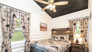 A bedroom with a wooden headboard, a bed with a patterned quilt, a nightstand with a lamp, and curtains with animal prints.
