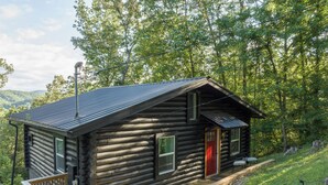 A log cabin with a wooden deck, a red door, and a metal roof.
