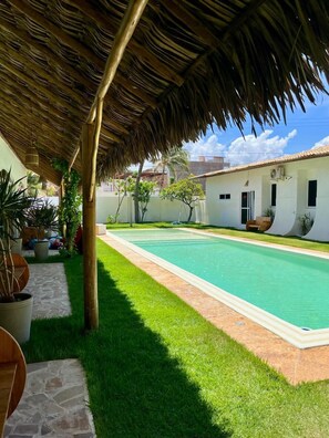 A pool area with a thatched roof, surrounded by a well-maintained lawn and potted plants. - Pousada Vila Flow (Caucaia)